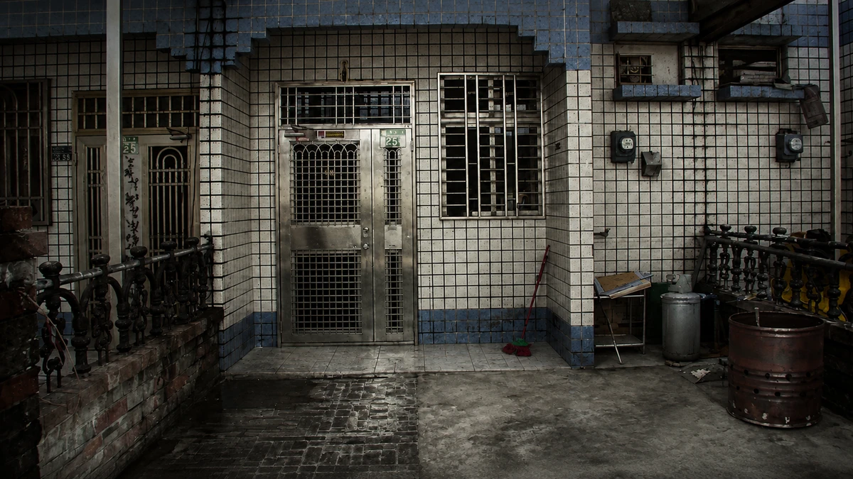 The tiled row house on Jichang First Street in dim light: a barred stainless-steel door with house number 25 beside it, iron window grilles, and a wet concrete forecourt